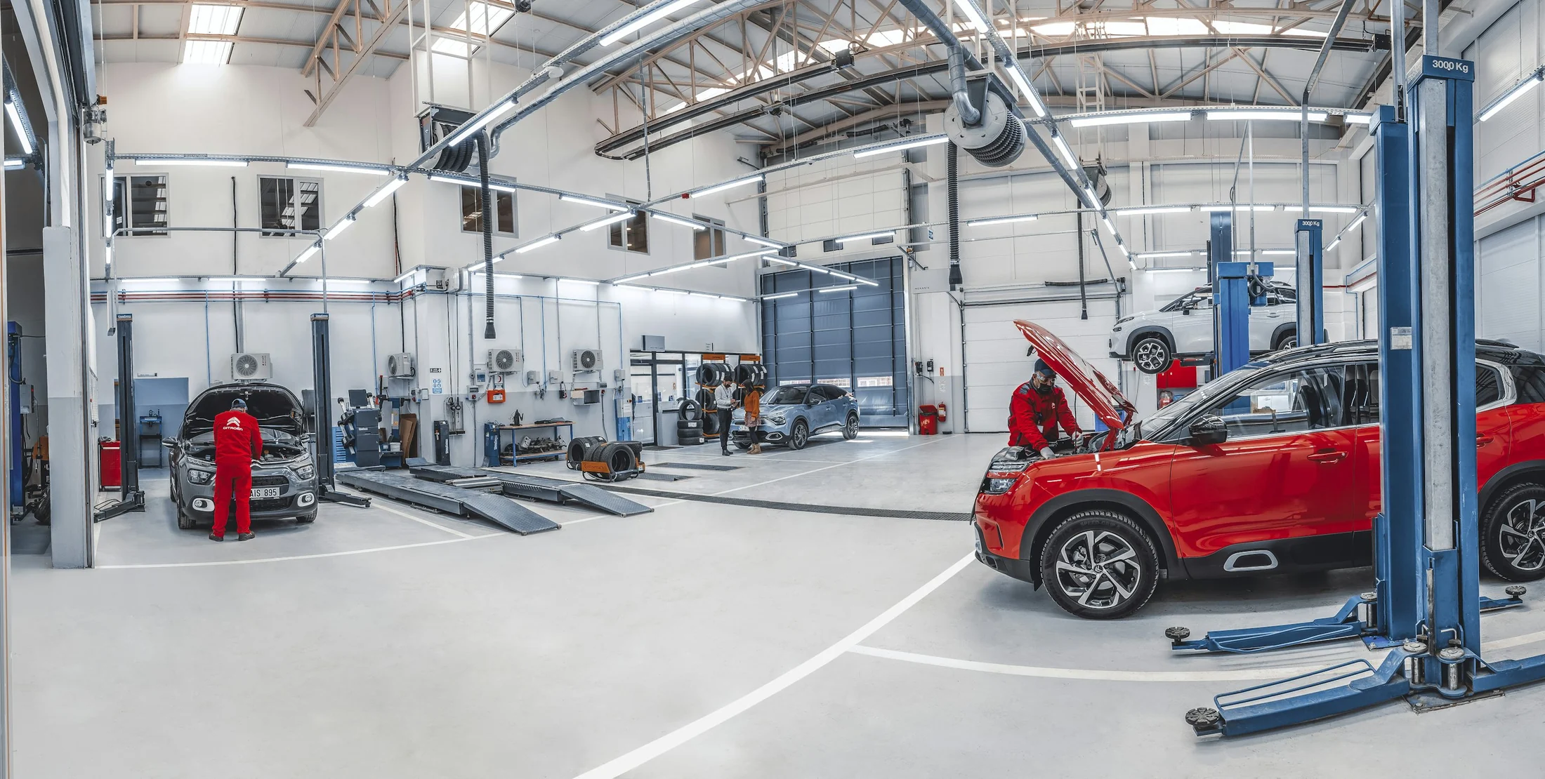 Moderne KFZ-Werkstatt mit Fahrzeugen, Hebebühnen und Technikern